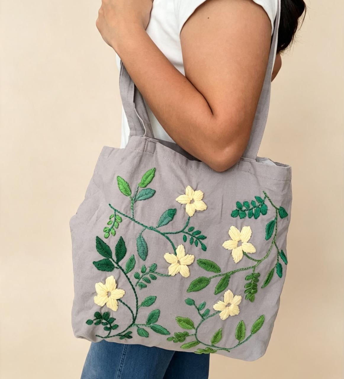 Bolsa de tela gris con hojas verdes y flores amarillas bordadas